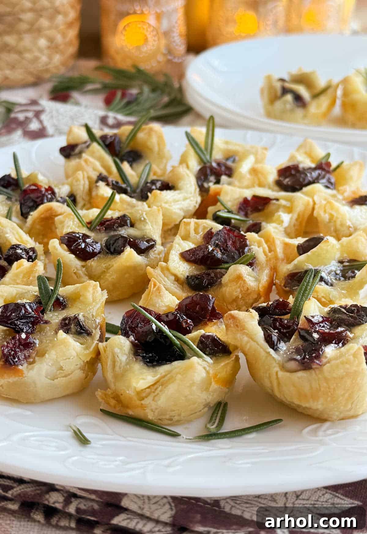 Golden cranberry brie bites baked in puff pastry, garnished with dried cranberries and fresh rosemary, ready to serve.