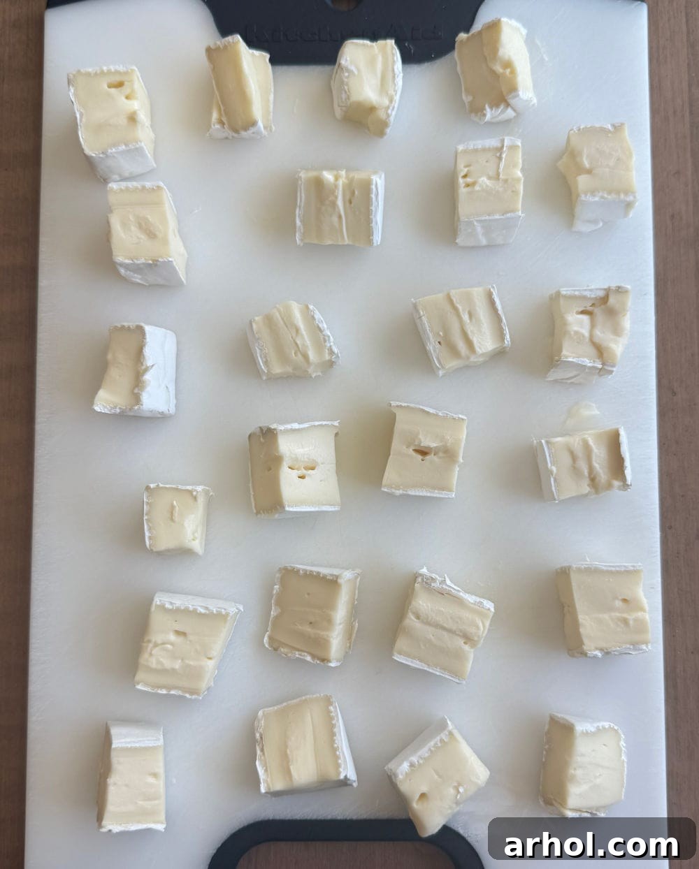 Brie cheese wheel cut into neat, uniform cubes ready for assembly.