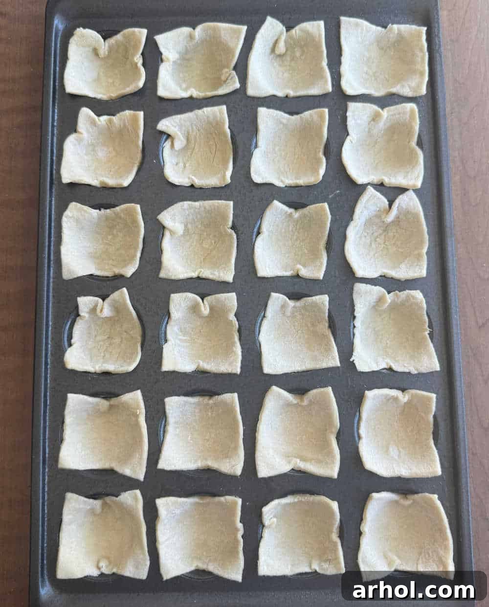 Puff pastry squares pressed into a mini muffin tin, prepared for the first bake.
