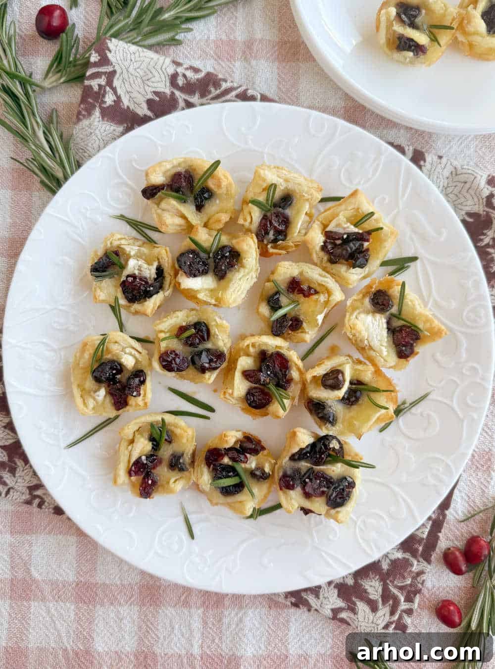 A plate of freshly baked cranberry brie bites, garnished with green rosemary sprigs.