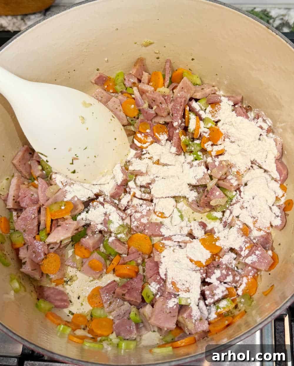 Stirring flour into sautéed vegetables and diced ham in a Dutch oven to create a roux.