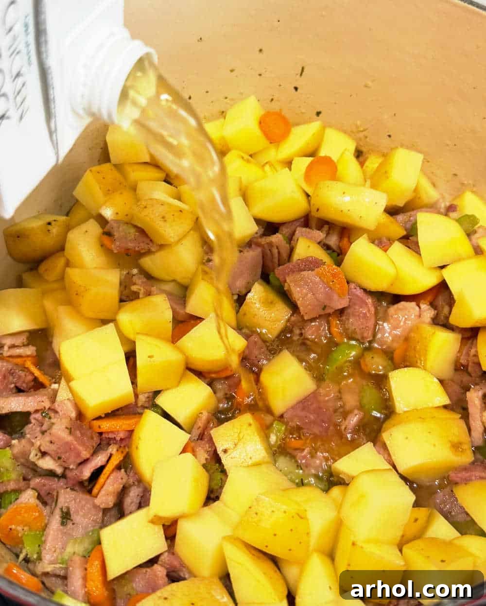 Adding cubed potatoes and chicken broth to the ham and vegetable mixture in a Dutch oven.