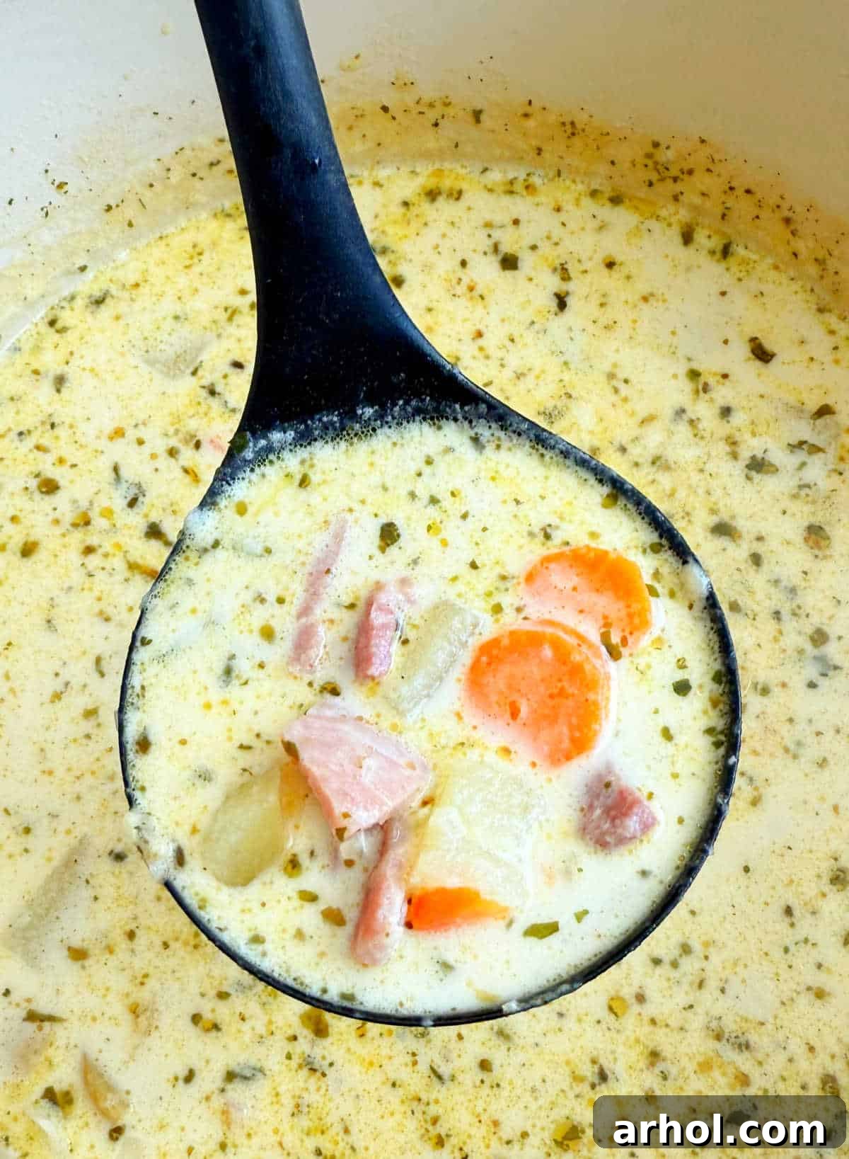 A ladle scooping creamy ham and potato soup from a large Dutch oven, showing the rich texture and ingredients.
