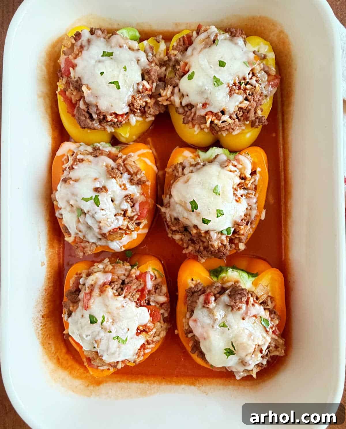 Grandma's Signature Stuffed Peppers 2 bell peppers stuffed with beef and rice with tomato sauce in baking dish.