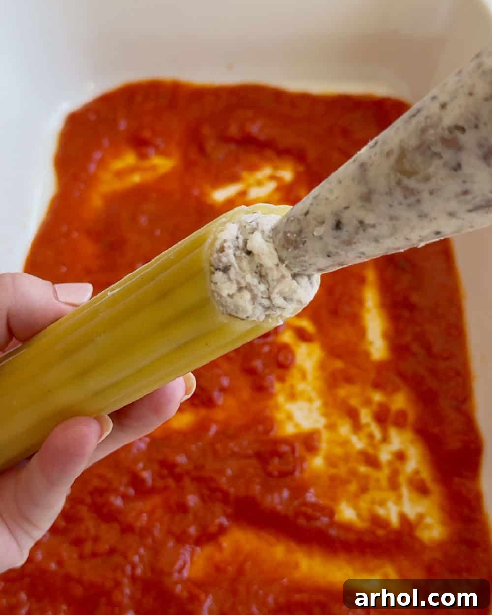 Stuffing cooked manicotti pasta shells with the meat and cheese filling using a piping bag for precision.