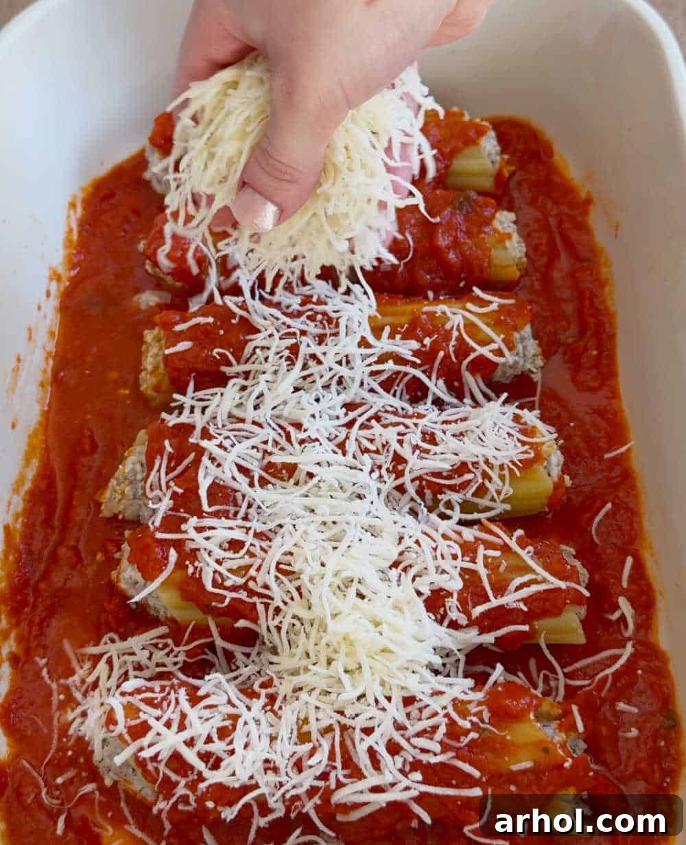 Manicotti arranged in a baking dish, topped generously with marinara sauce and shredded cheese, ready for the oven.