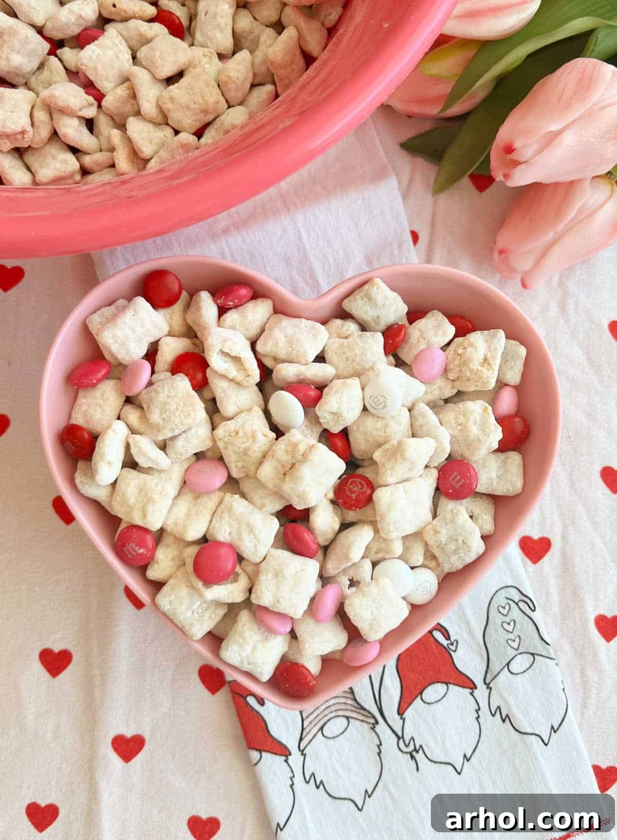 Valentine's Day puppy chow in a pink heart bowl, adorned with festive pink and red candies.