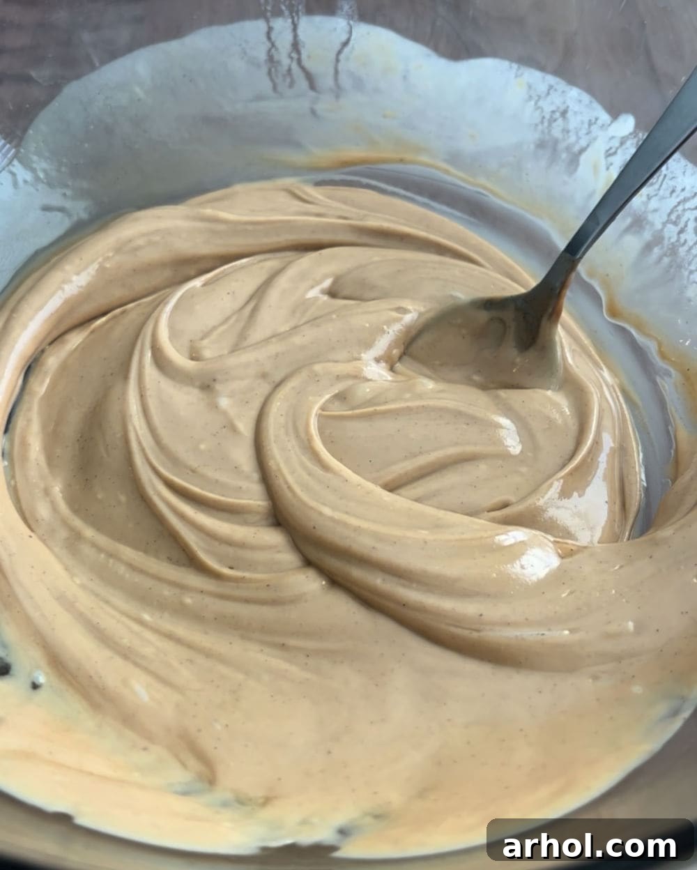 Melted white chocolate, peanut butter, and butter being stirred in a large bowl, ready for cereal.