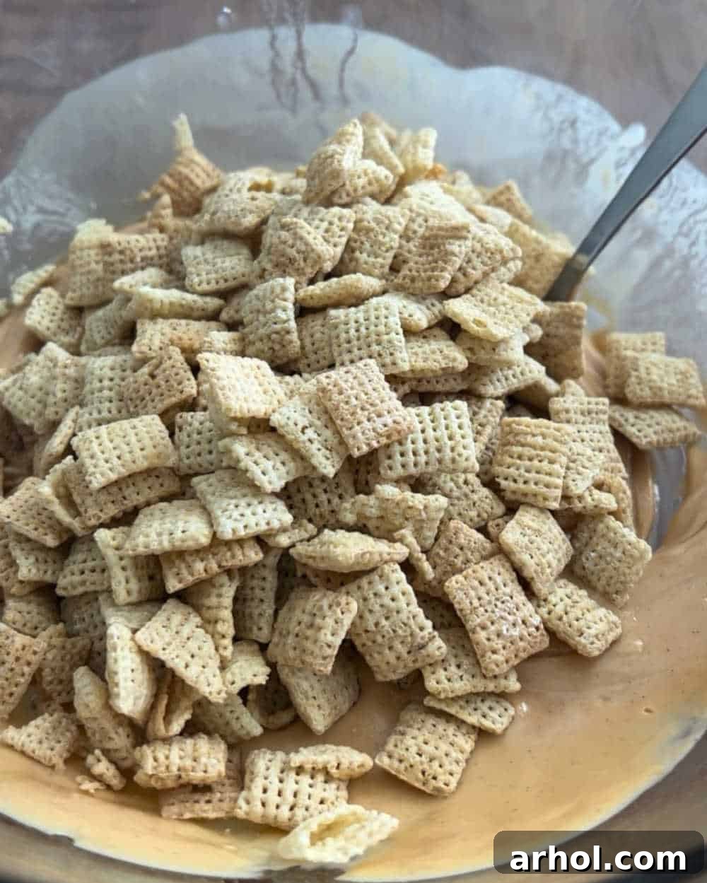 Rice Chex cereal being added to the melted chocolate and peanut butter mixture in a bowl.