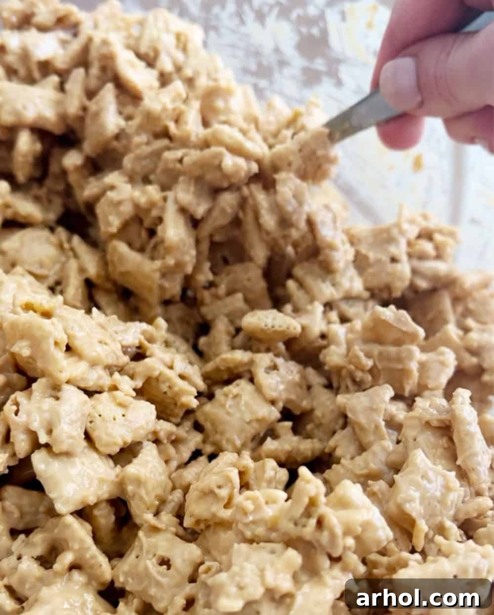 A spoon gently mixing Chex cereal with the chocolate coating to ensure even coverage.