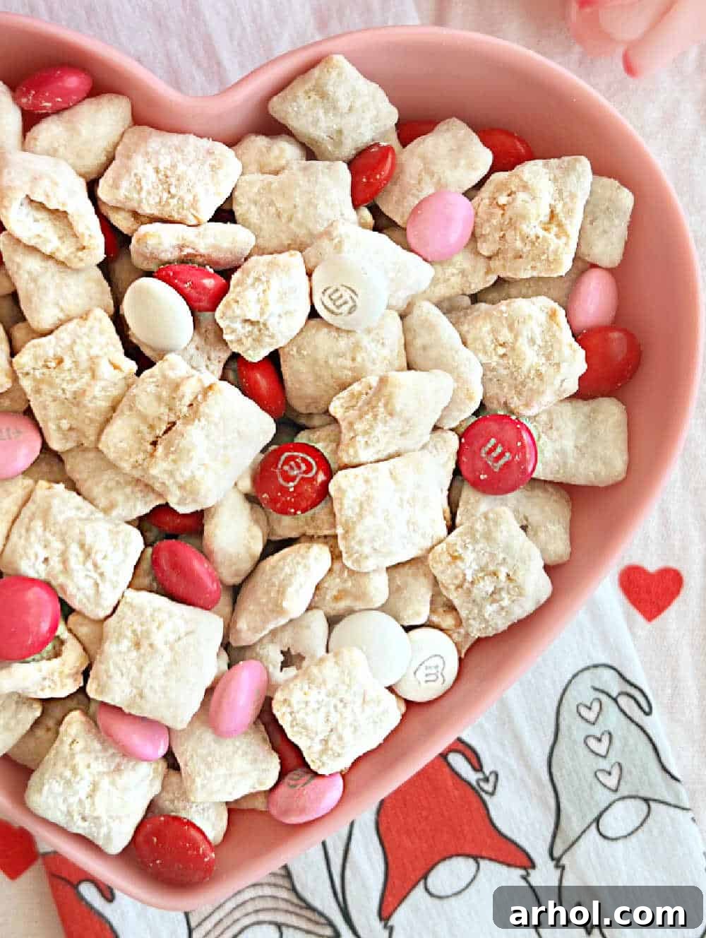 Valentine's Day muddy buddies served in a pink heart-shaped bowl, ready to be enjoyed.