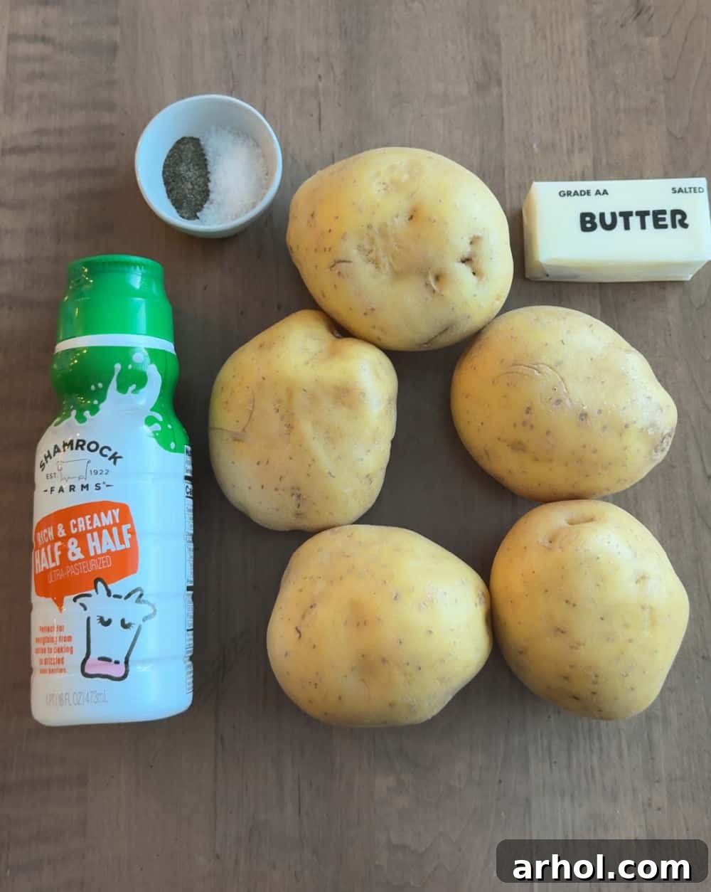 Fresh Yukon Gold potatoes, rich cream, golden butter, and essential seasonings laid out on a rustic surface, ready for mashing.
