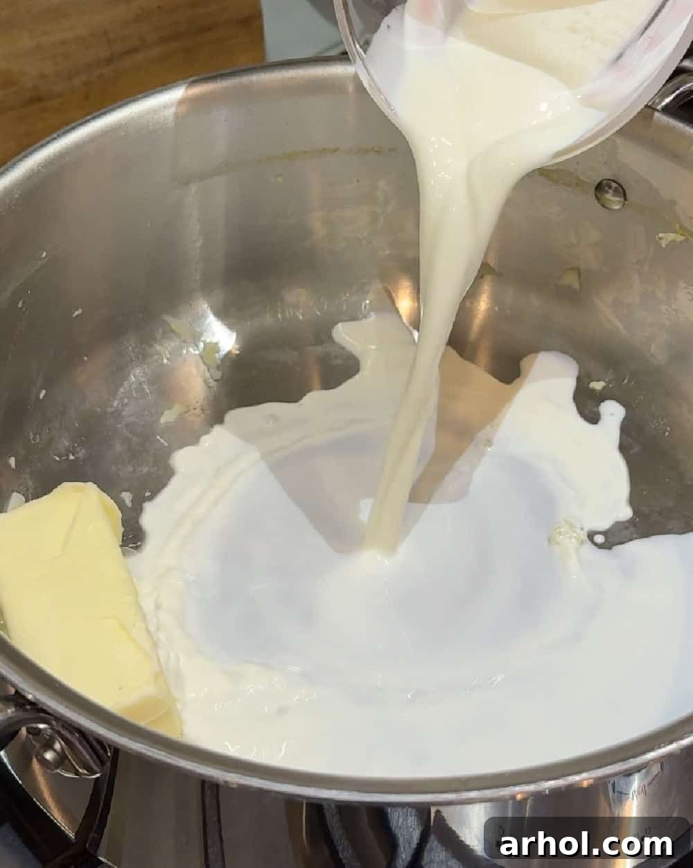 Rich half and half being poured into a pot of freshly drained, hot potatoes, preparing for the mashing process.