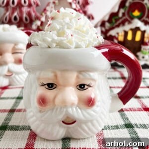 A Santa mug filled with rich peppermint hot cocoa, topped generously with whipped cream and sprinkled with crushed candy canes, a perfect festive drink for the holidays.