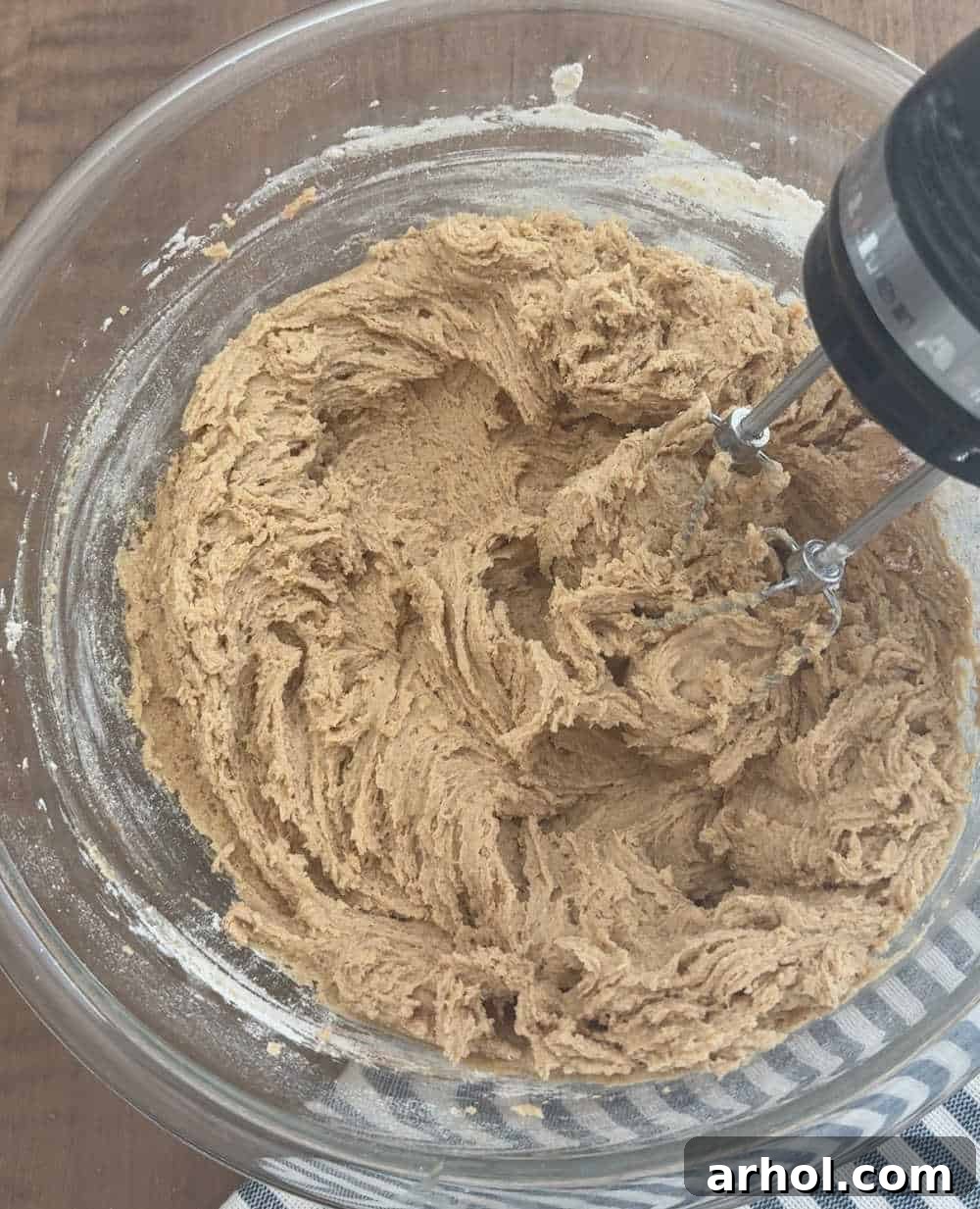 Mixing the cookie dough with a hand mixer, ensuring all wet ingredients are well combined.