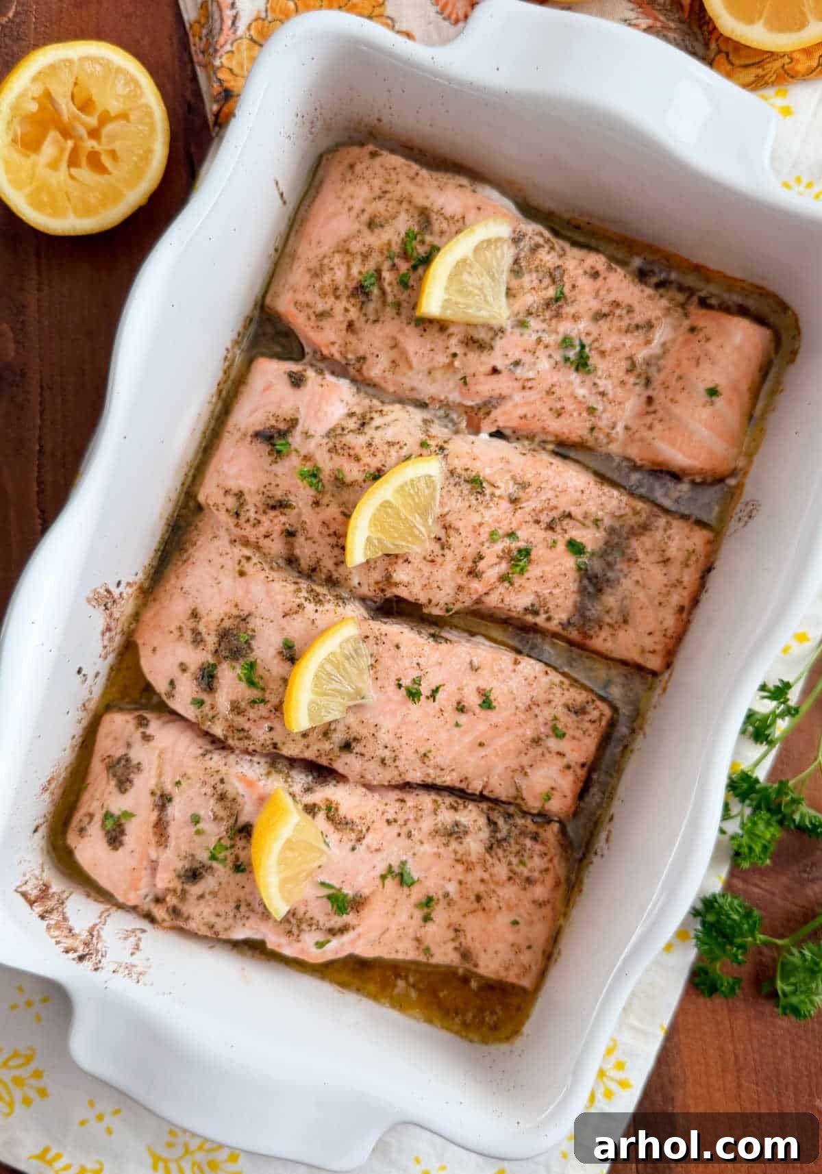 baked salmon with lemon slices in garlic butter in baking dish.