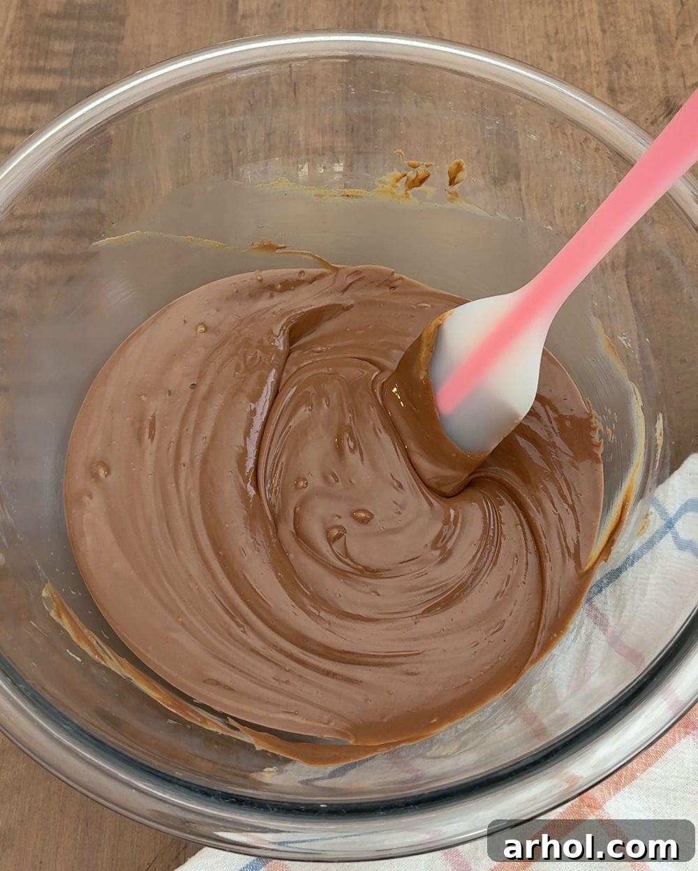 Stirring melted chocolate and creamy peanut butter together in a glass bowl to achieve a smooth consistency.