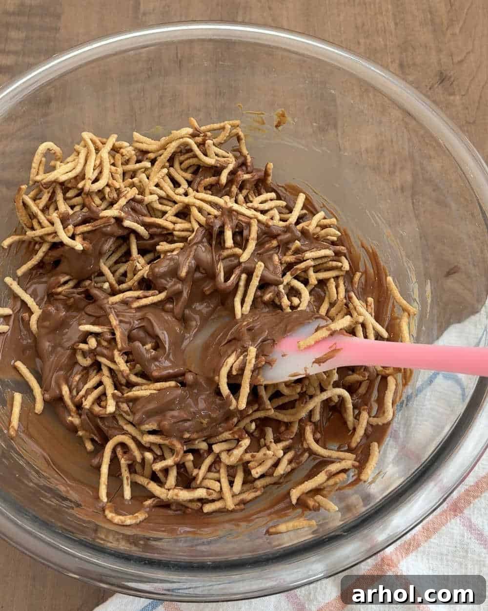 Gently stirring crunchy chow mein noodles into the melted chocolate and peanut butter mixture.