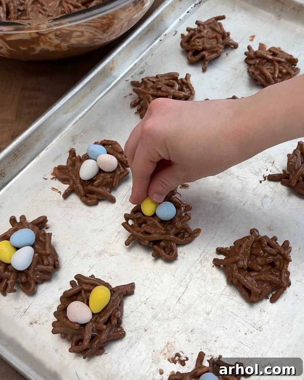 Placing colorful mini candy eggs into the center of freshly formed chocolate bird's nest cookies.