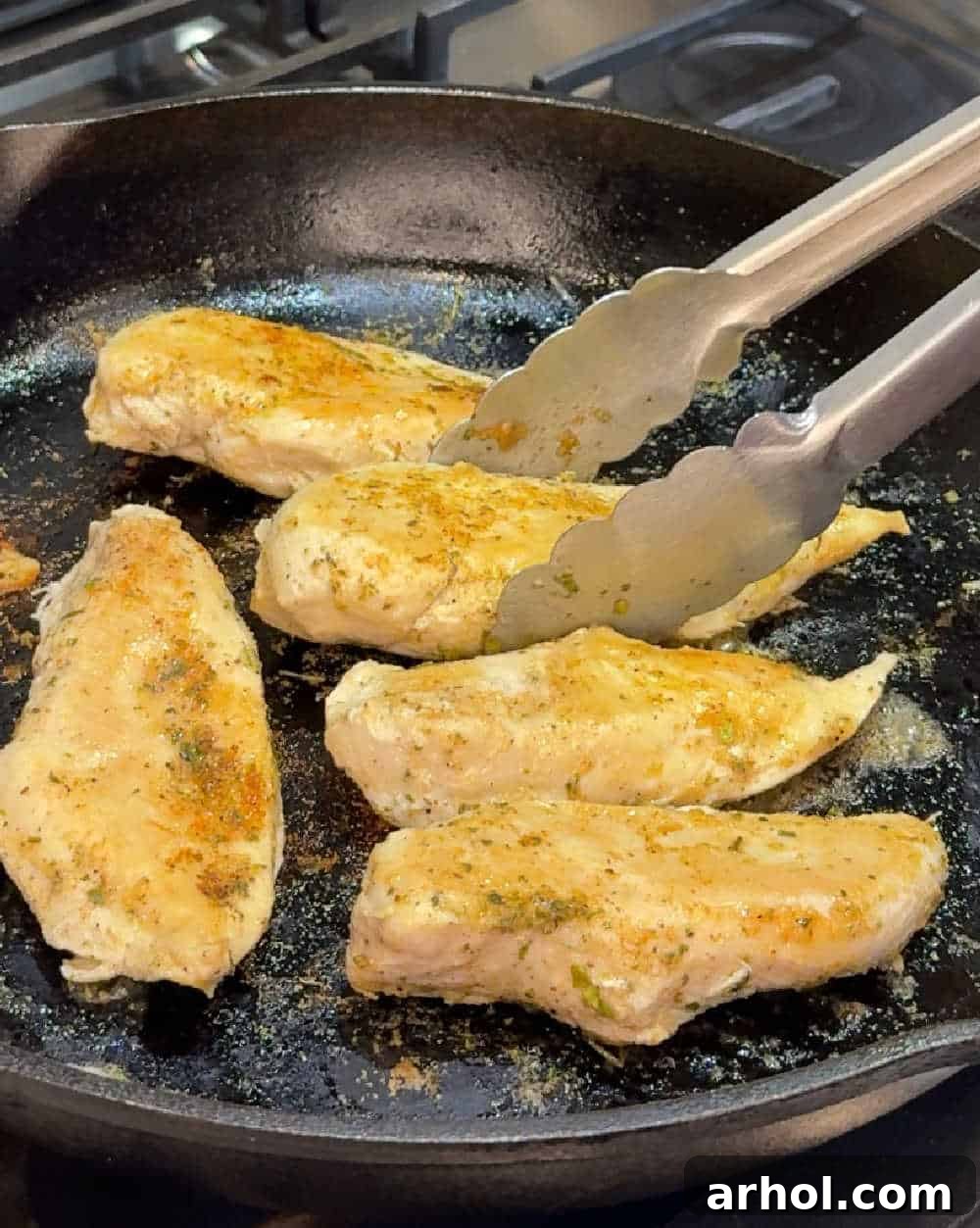 Browned chicken breast sizzling in a cast iron skillet.
