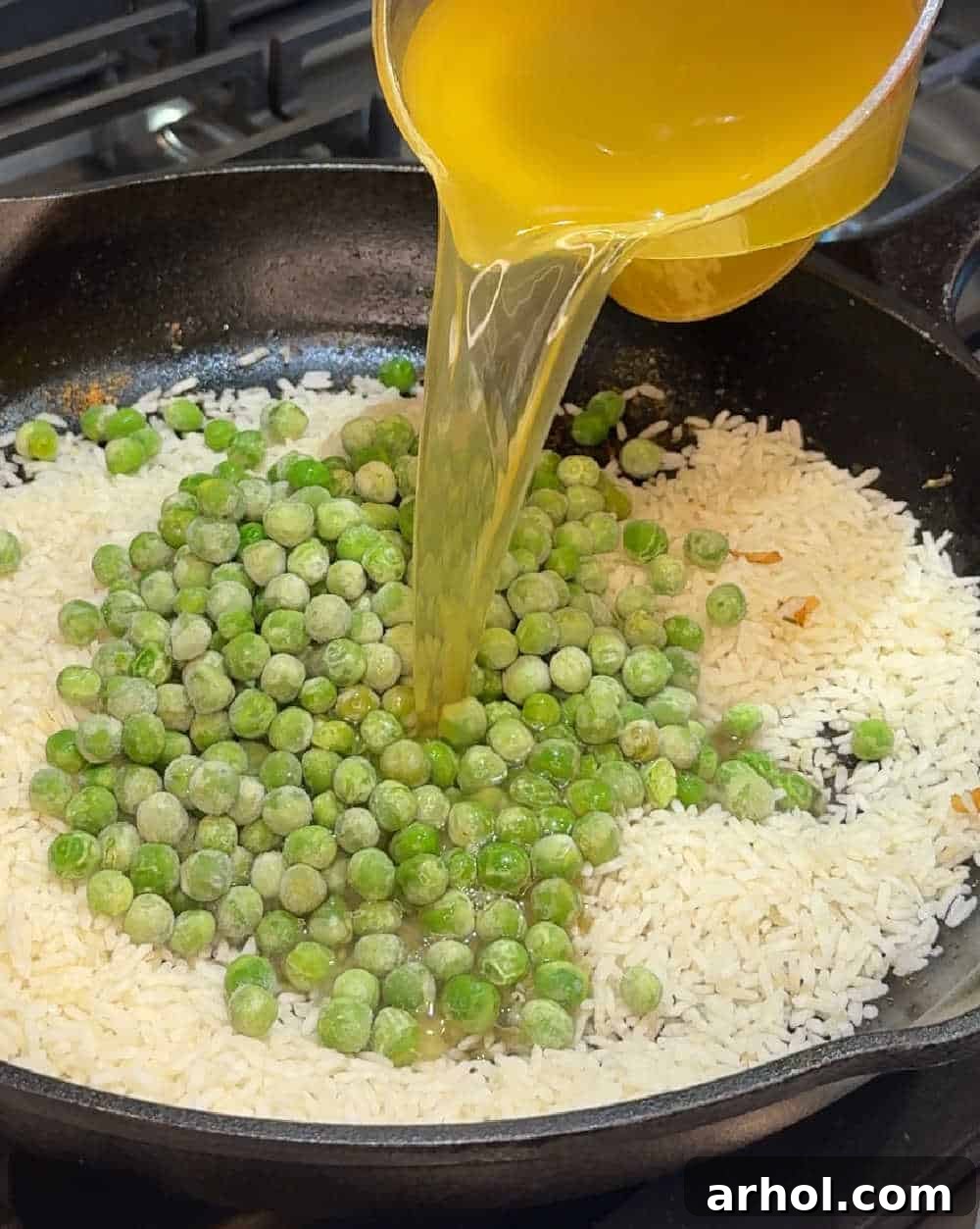 Adding chicken broth to instant rice and peas in a skillet.