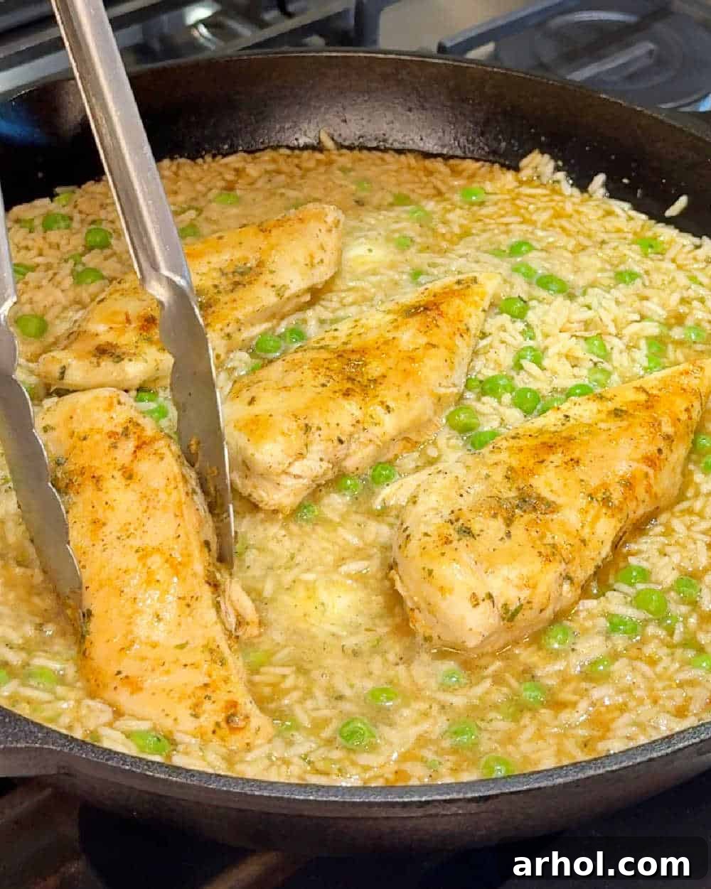Chicken breasts simmering with rice and peas in a covered skillet.
