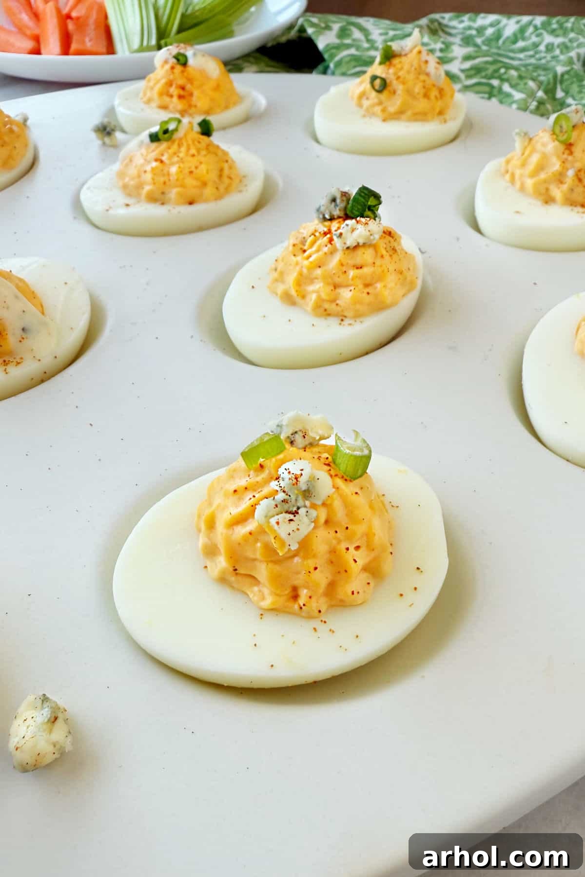A vibrant tray of Buffalo deviled eggs, garnished with fresh carrot and celery sticks, beautifully arranged for a party spread.
