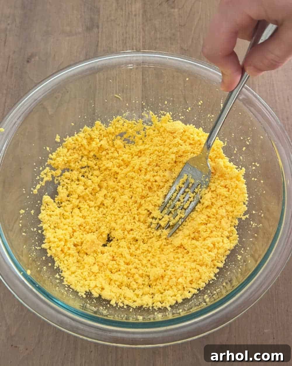 A fork mashing bright yellow egg yolks in a mixing bowl, creating a smooth base for the filling.