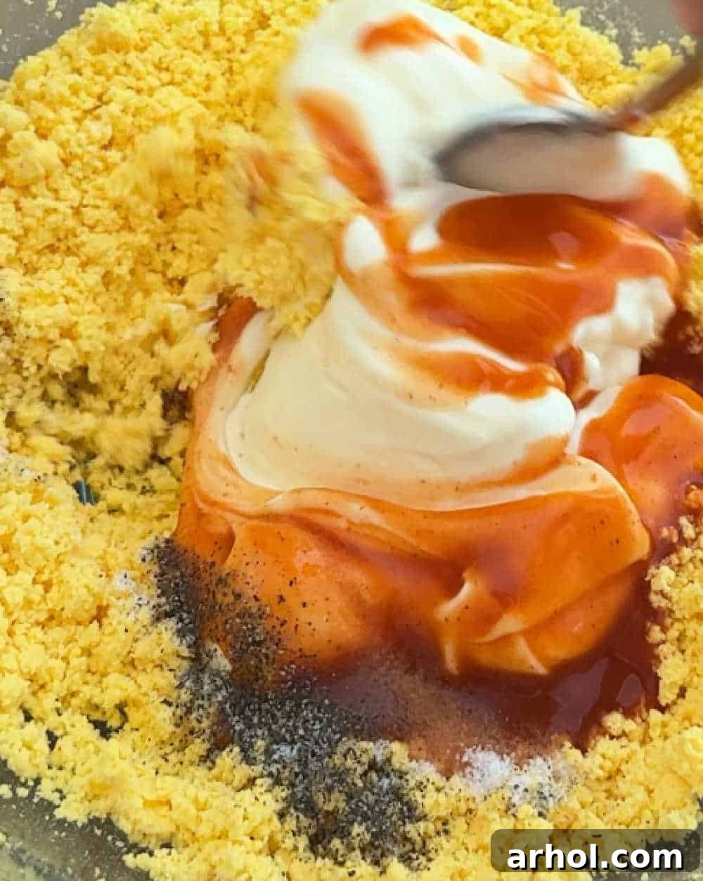 The creamy yolk mixture, blended with mayonnaise and Buffalo sauce, being stirred in a bowl.