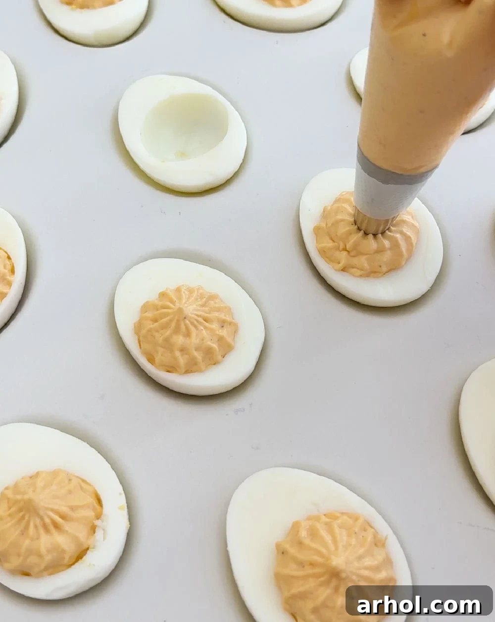 A piping bag expertly filling egg white halves with the spiced yolk mixture, creating perfectly shaped deviled eggs.