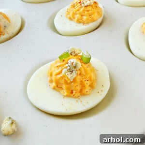 Buffalo deviled eggs topped with paprika, fresh chives, and crumbled gorgonzola cheese, perfectly presented on a white serving dish.