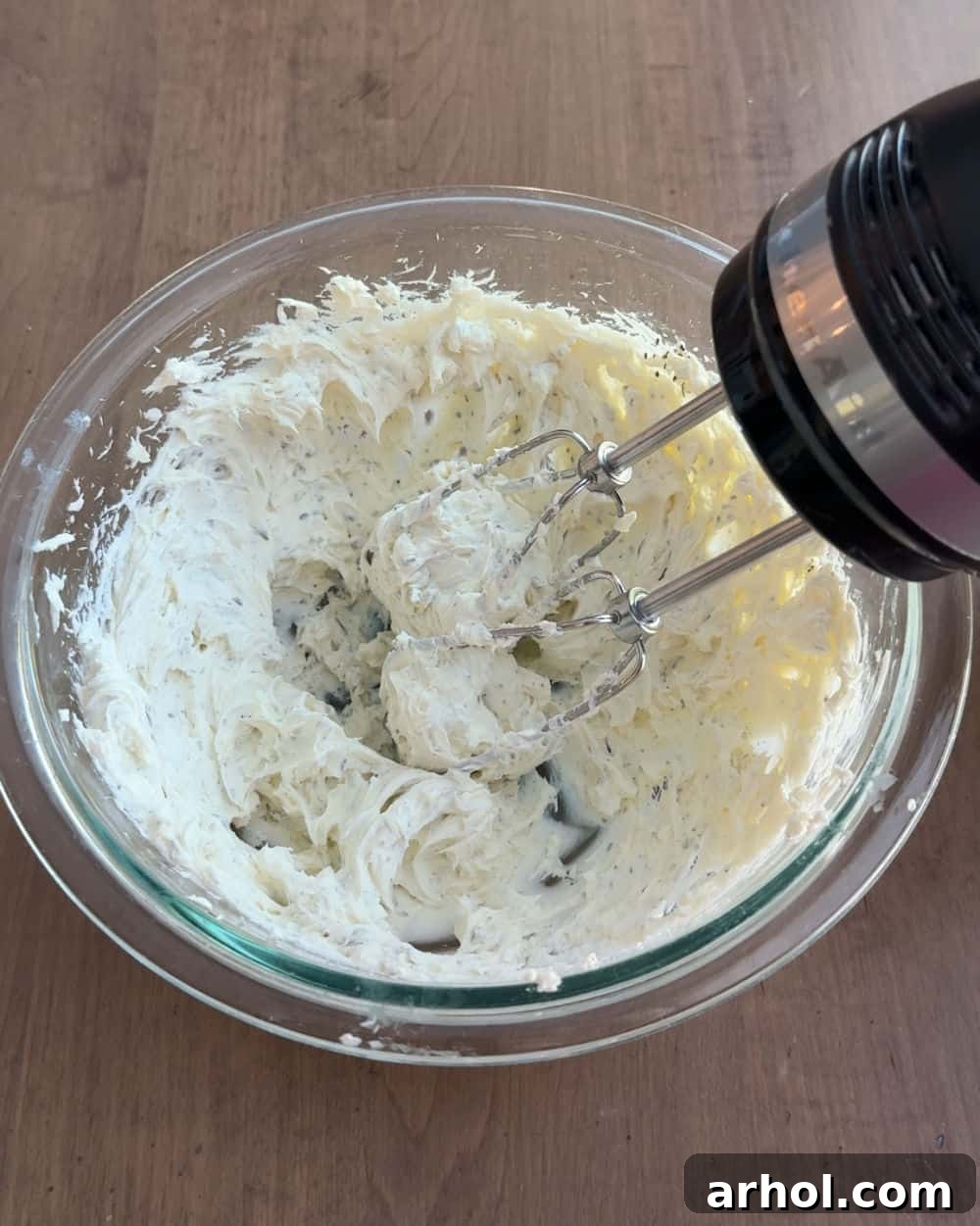 An electric mixer actively blending cream cheese and seasonings in a mixing bowl until smooth and fluffy.