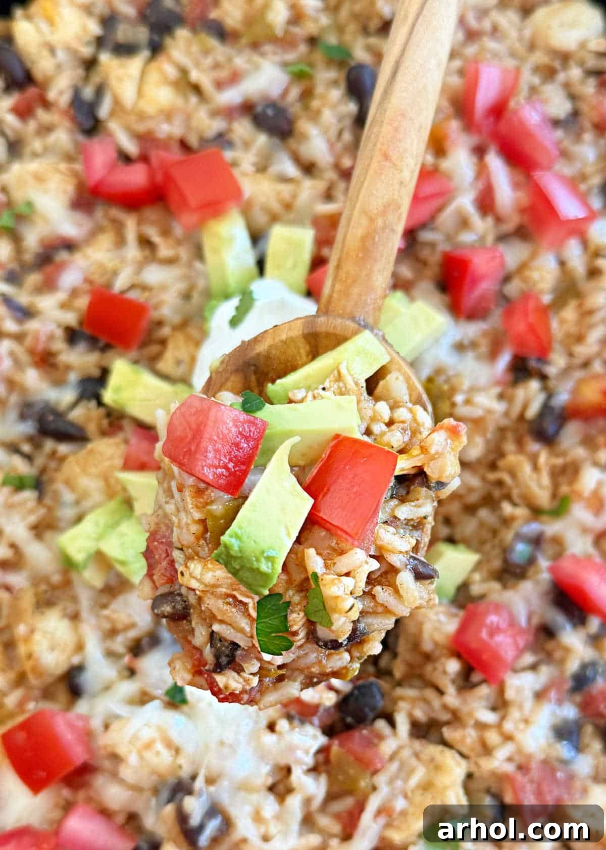 One Pan Mexican Chicken and Rice with black beans, tomatoes, and avocado on a serving spoon, garnished with fresh cilantro.