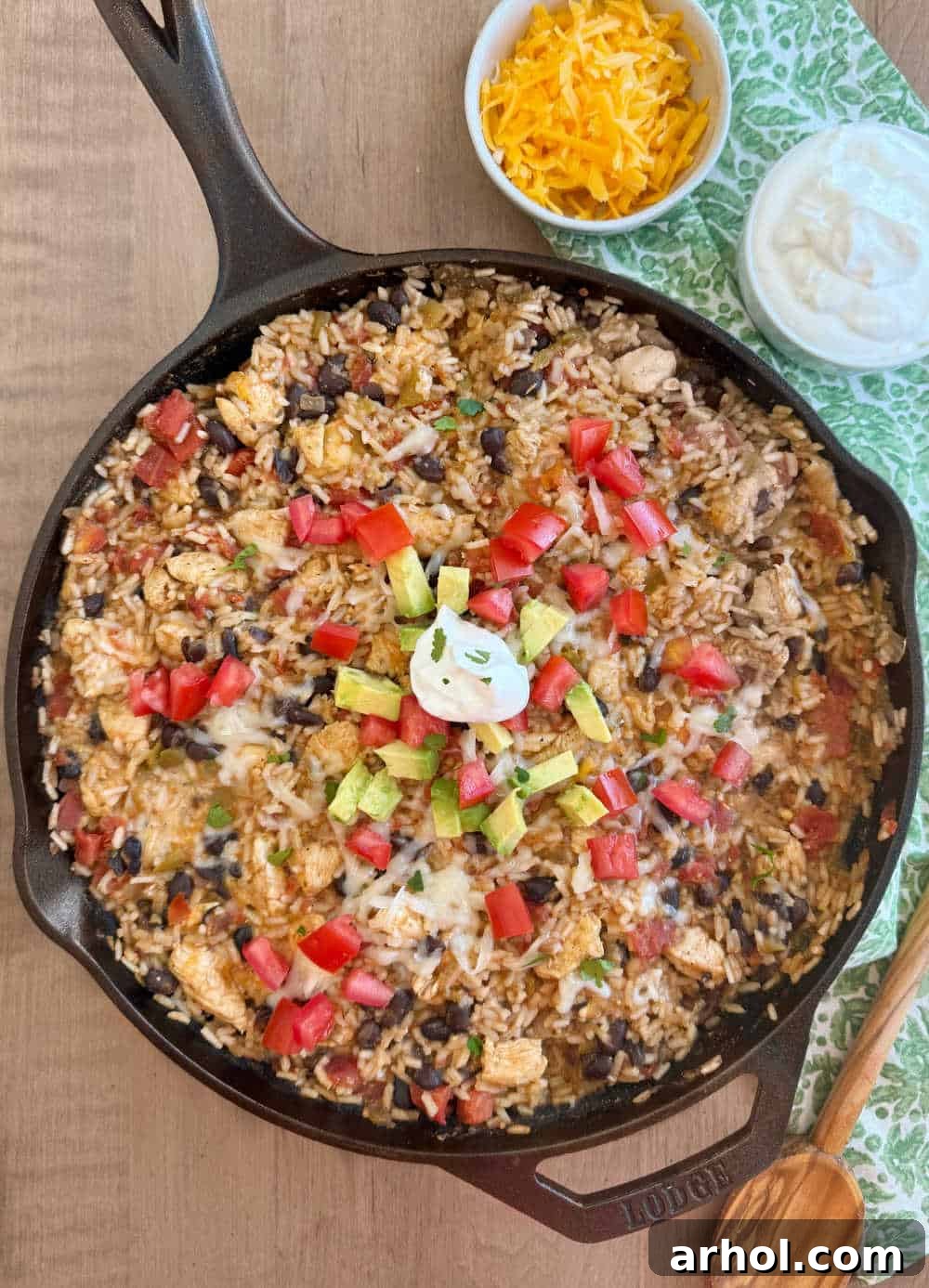 One Pan Mexican chicken and rice served in a cast iron skillet with various taco toppings arranged around it, including avocado, sour cream, and cilantro.