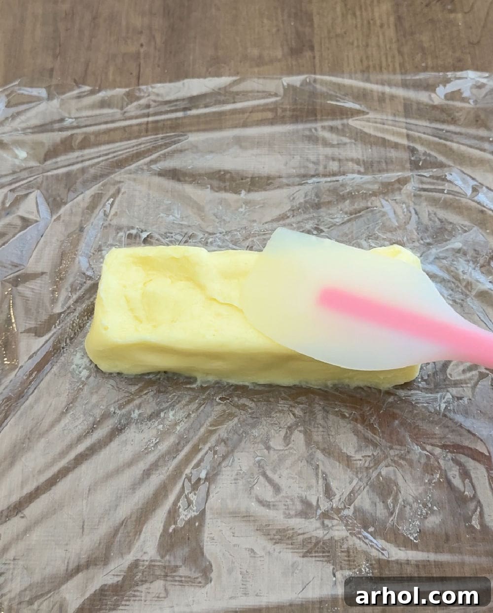 A person shaping fresh homemade butter into a neat stick on a piece of plastic wrap, ready for storage.