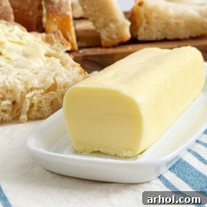 A stick of golden homemade butter resting on a white butter dish.