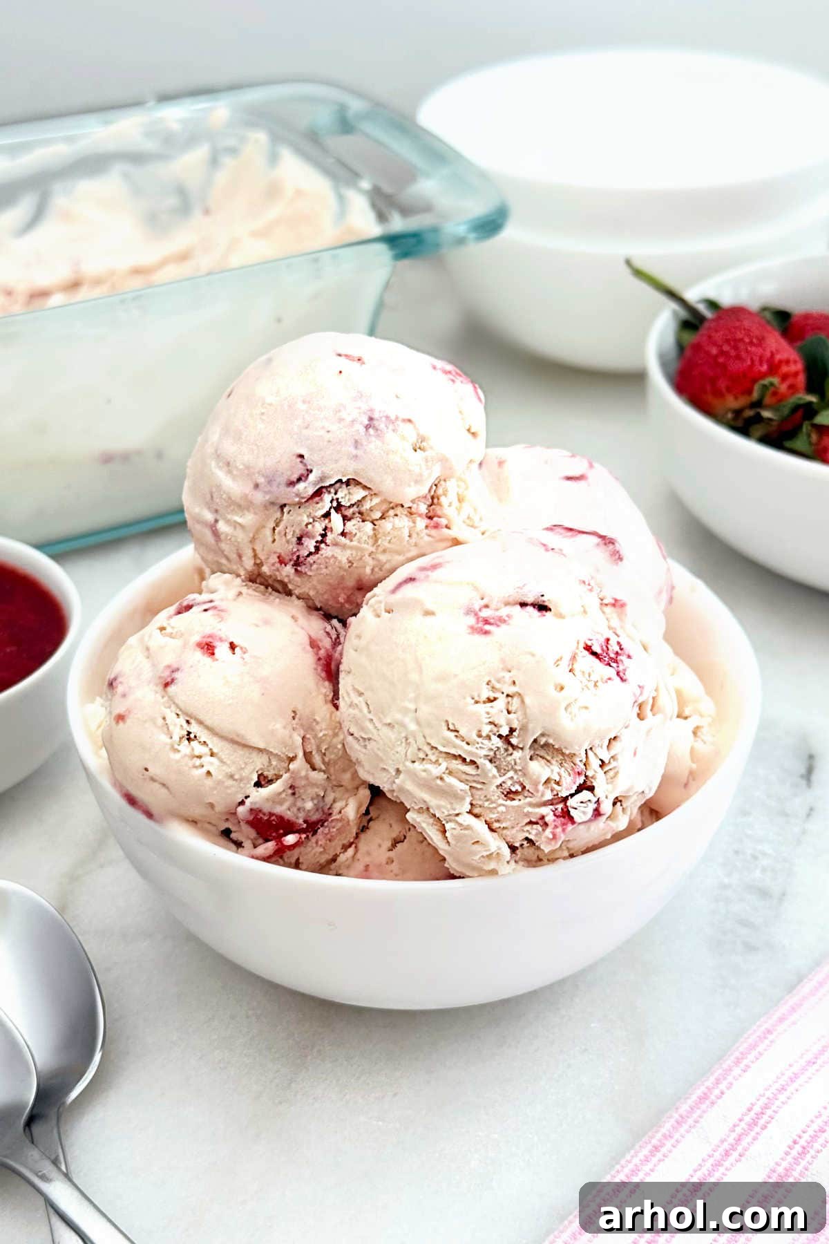 homemade strawberry ice cream in a white bowl, garnished with fresh strawberries.