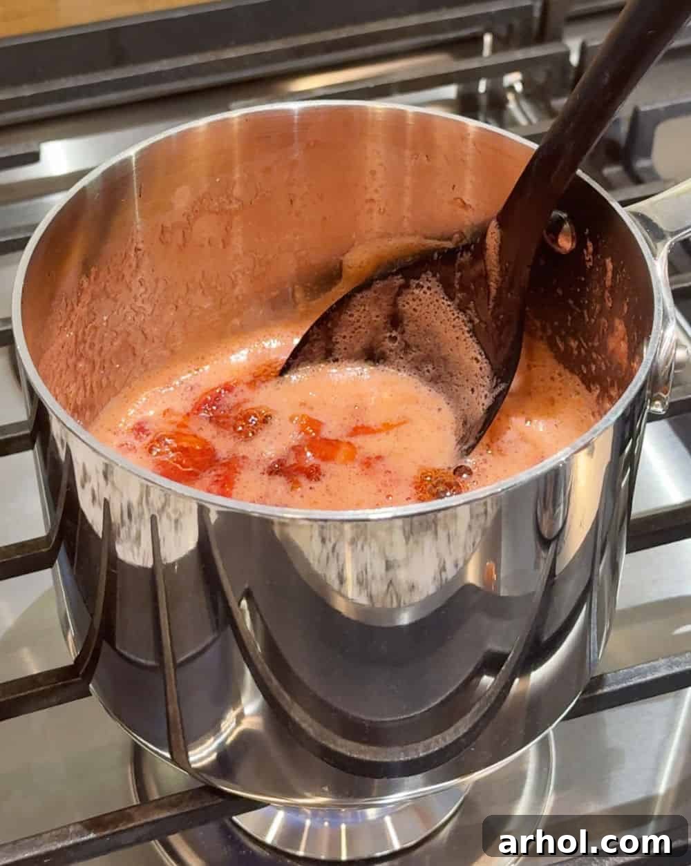 Strawberries, sugar, and lemon juice cooking in a saucepan on the stove.