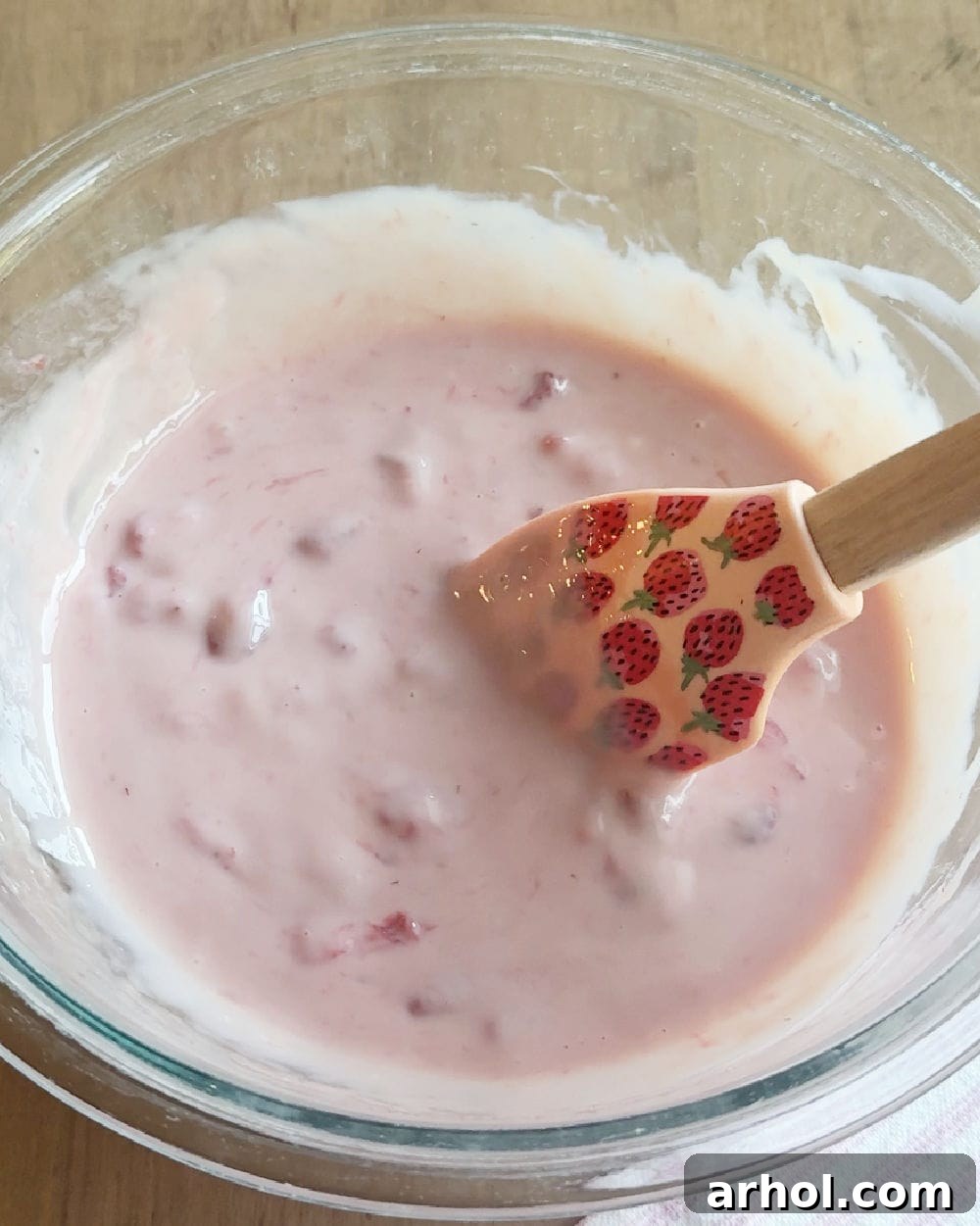 Stirring cooked strawberry mixture with sweetened condensed milk in a bowl.