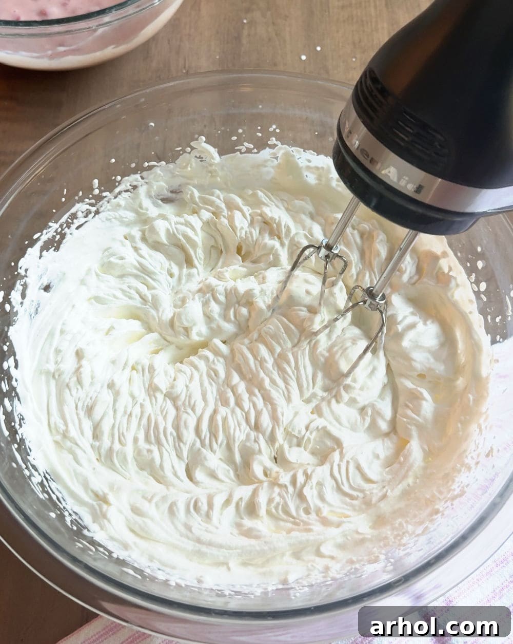 Electric mixer whipping heavy cream to stiff peaks in a bowl.