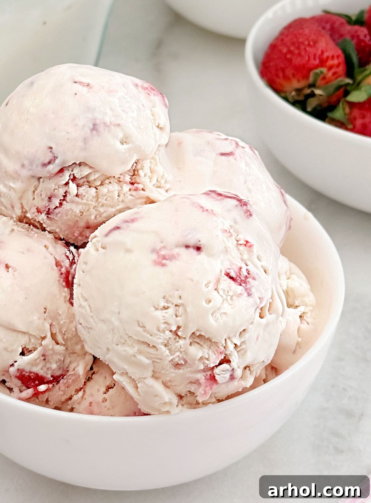 scoops of no churn strawberry ice cream in a white bowl, garnished with mint.