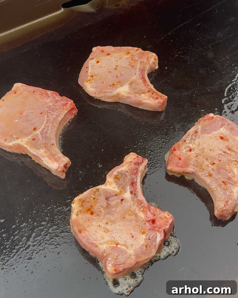 Bone-in rib chops sizzling on a hot griddle.