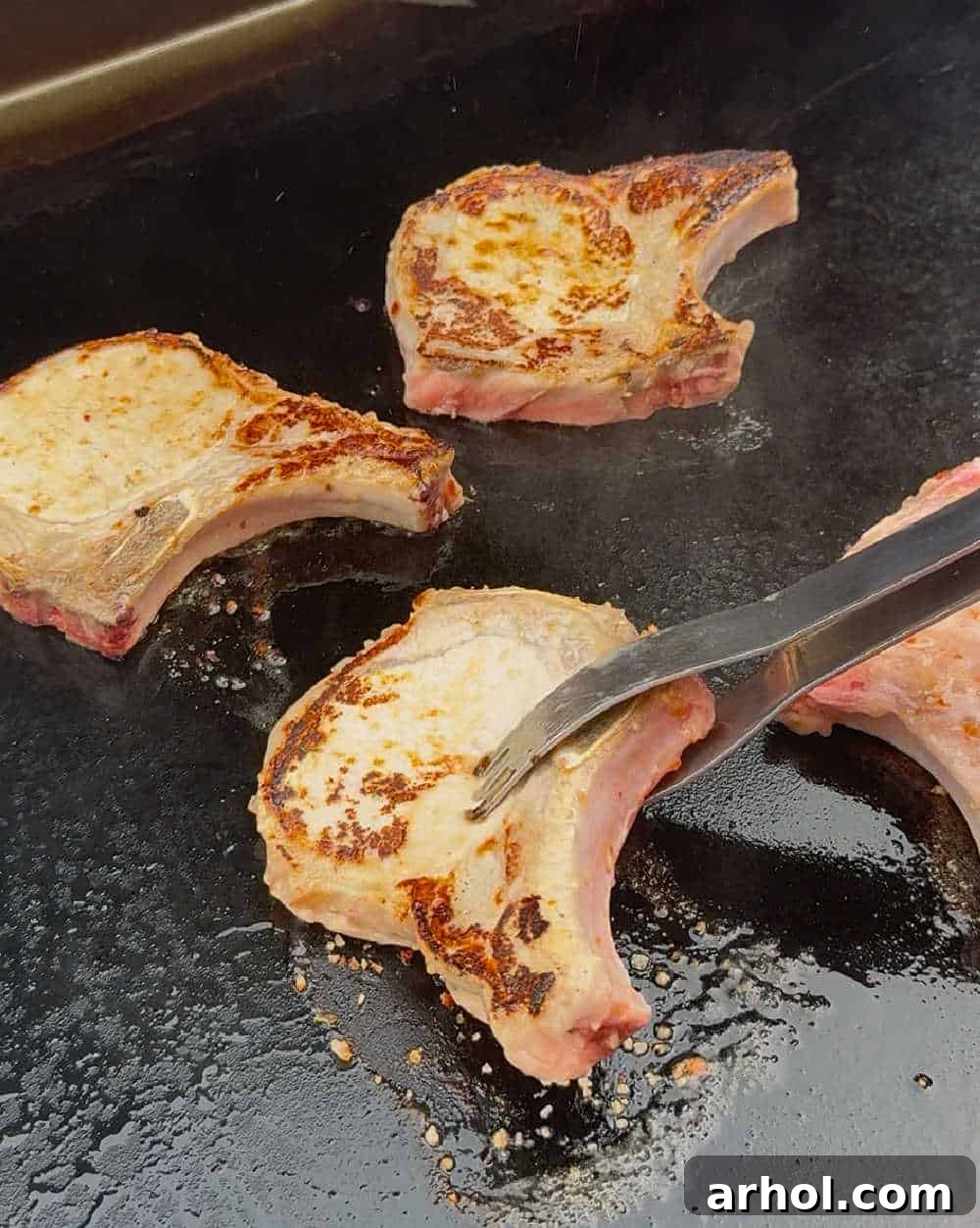 Flipping pork chops with BBQ tongs on the griddle.