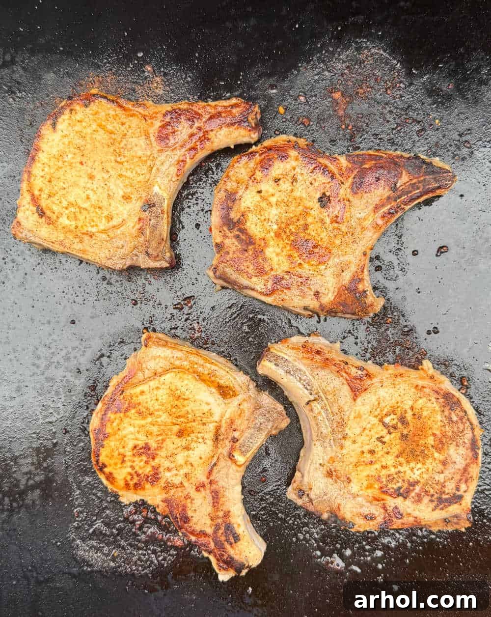 Two perfectly cooked pork chops resting on a Blackstone griddle.