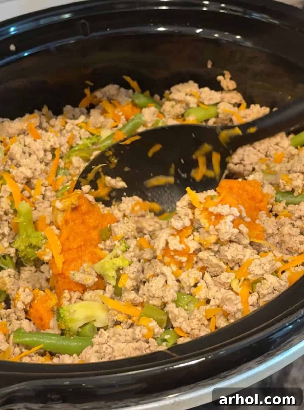 Stirring the cooked turkey and vegetable mixture in the slow cooker after adding pumpkin puree.