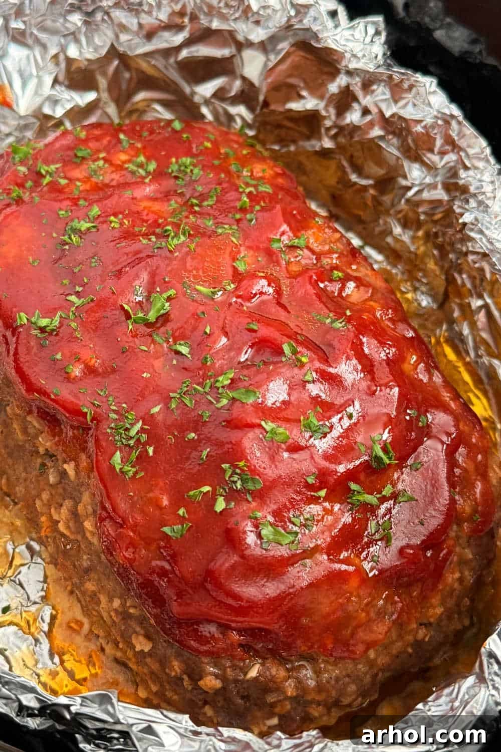 A perfectly cooked meatloaf in a slow cooker, wrapped in foil, ready to be served.