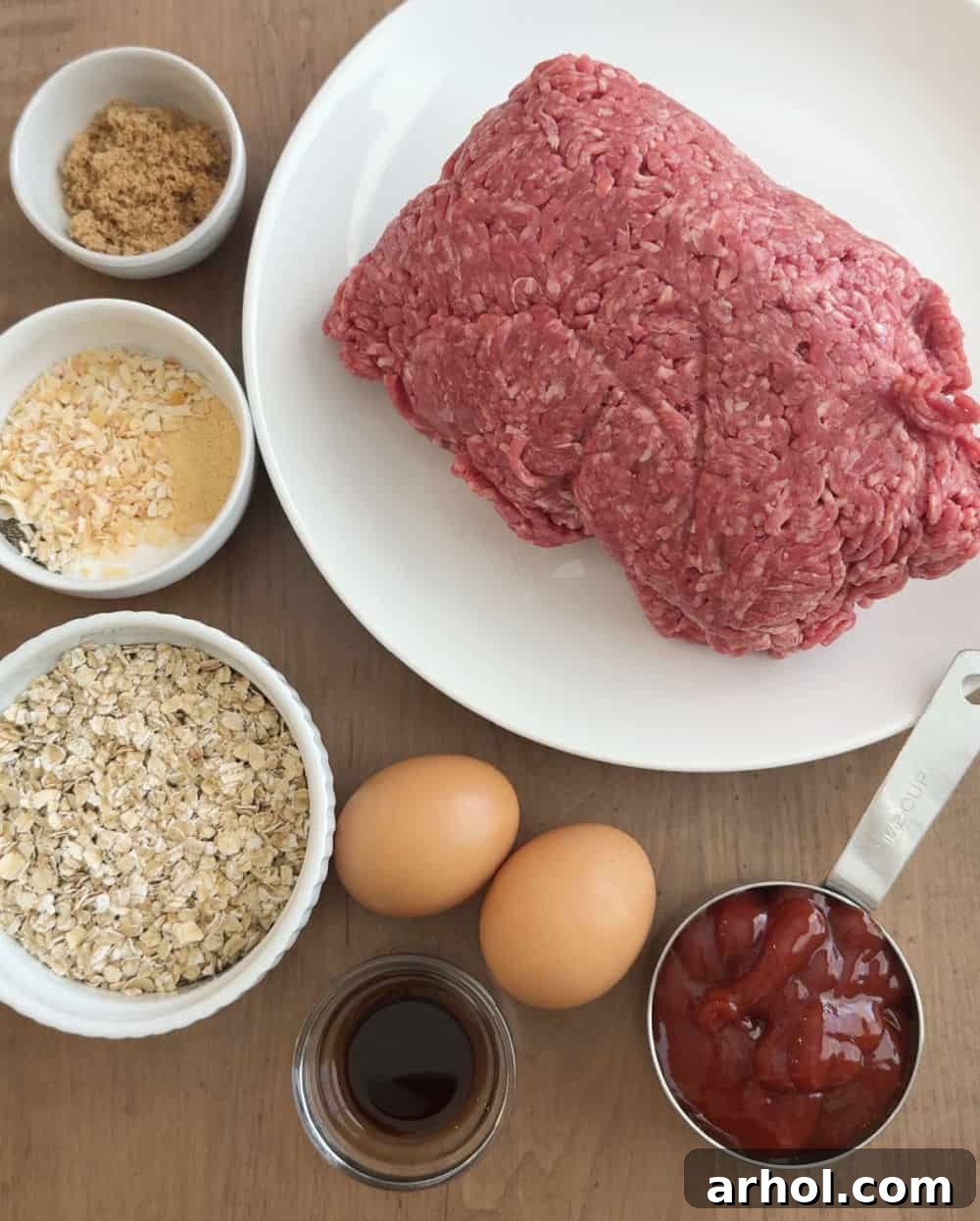 A collection of ingredients for meatloaf: ground beef, ketchup, eggs, oats, Worcestershire sauce, brown sugar, and various seasonings.