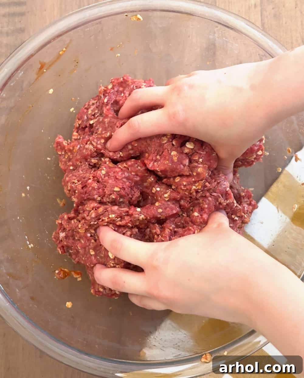 Hands gently mixing ground beef and other ingredients in a bowl for meatloaf.