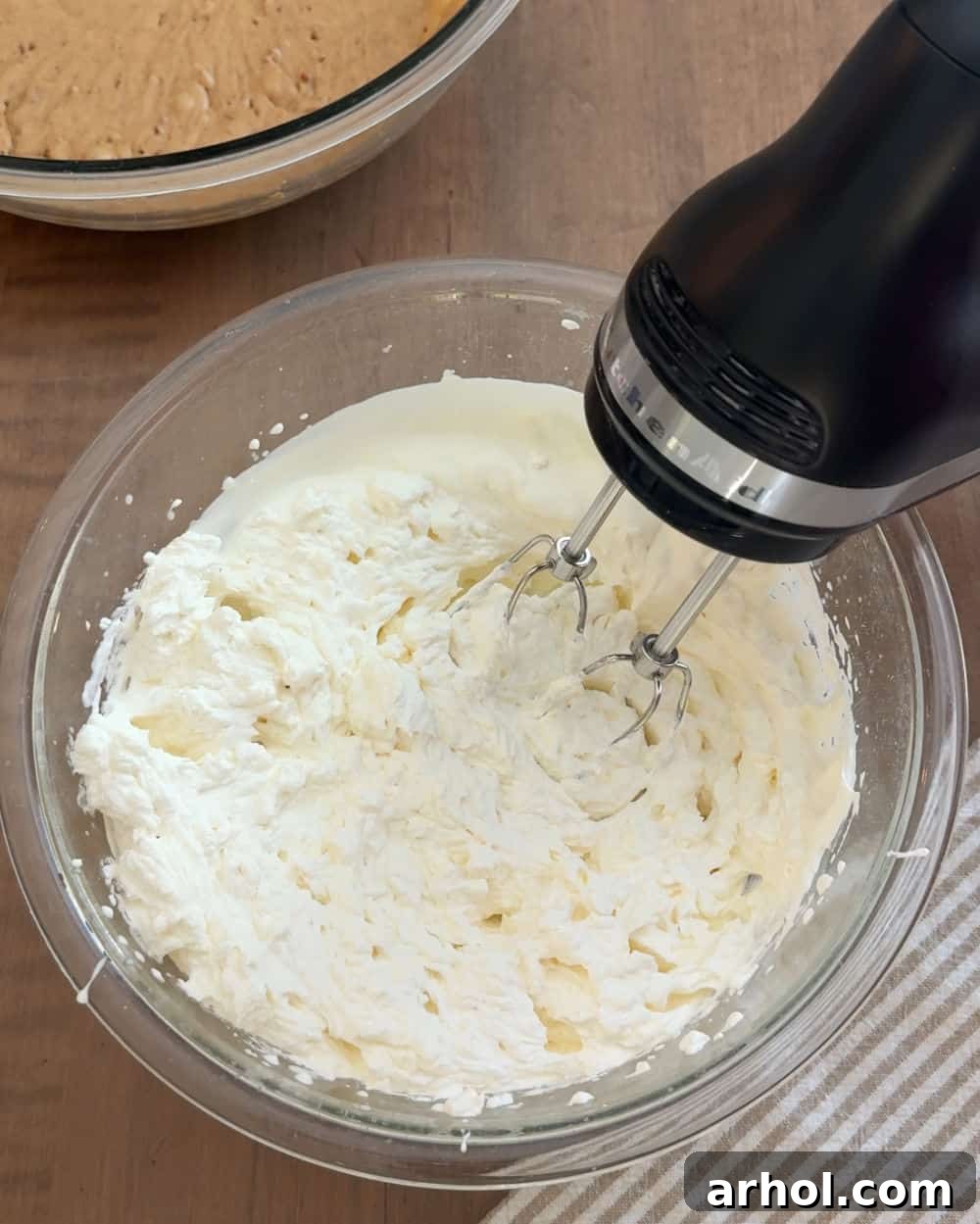 Electric mixer whipping heavy cream in a large mixing bowl until stiff peaks form.