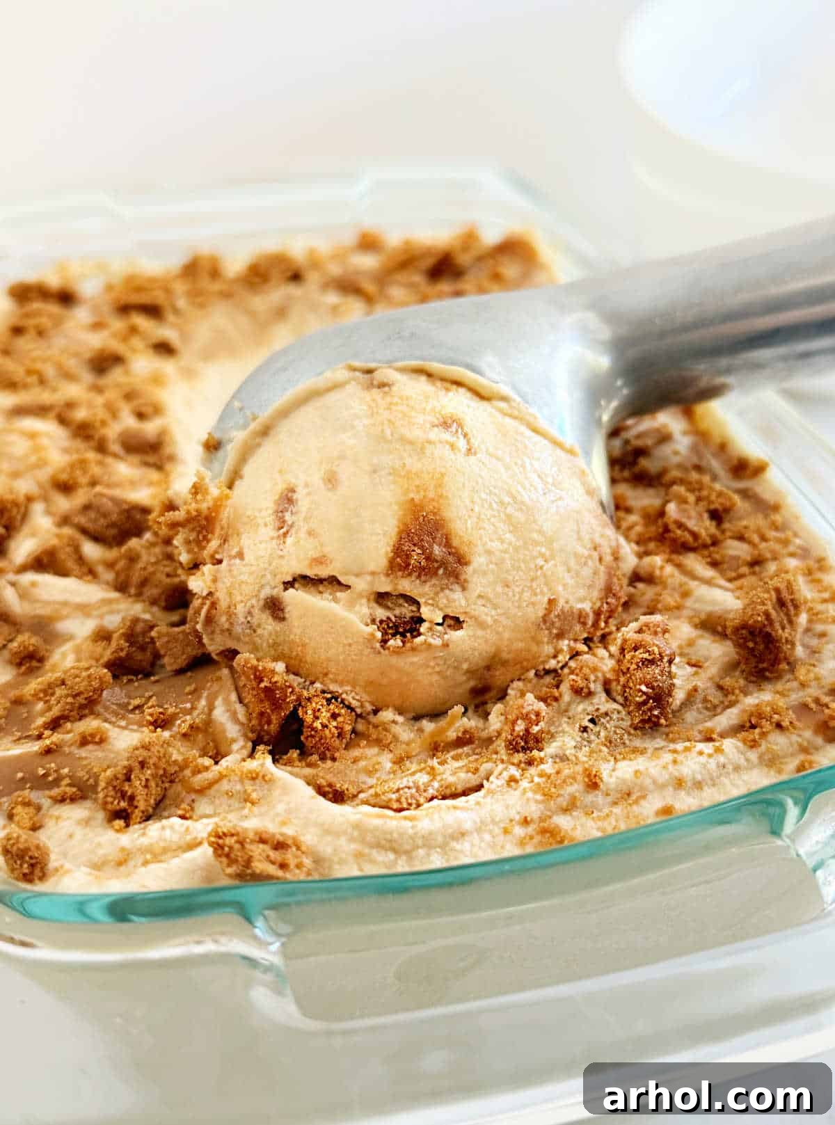 Ice cream scoop perfectly carving into a frozen block of Biscoff ice cream, revealing its creamy texture and cookie swirls.